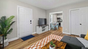 Una sala de estar con un sofá, una mesa de centro, un televisor y una cocina al fondo.