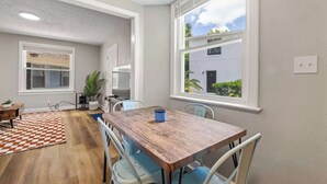 Un comedor con una mesa de madera, sillas azules, un tapete a cuadros y un ventanal con vistas a un edificio.