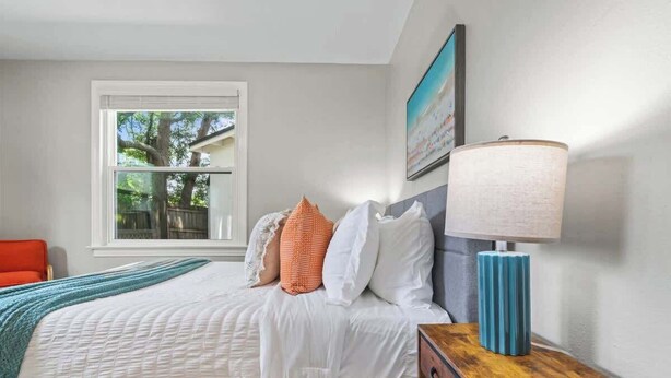 Un dormitorio con cama, almohadas, lámpara, ventana y una silla.