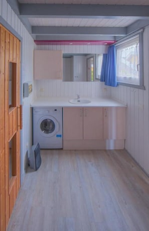 A compact, modern bathroom with a washing machine, sink, and wooden cabinets.