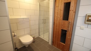 Une salle de bain avec des carreaux blancs, des toilettes, une douche avec des portes en verre et une porte en bois.