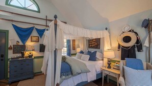 Een slaapkamer met een hemelbed, nachtkastje, stoel en nautische decoraties.