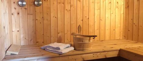 A wooden sauna with a bench, a wooden bucket, and towels.
