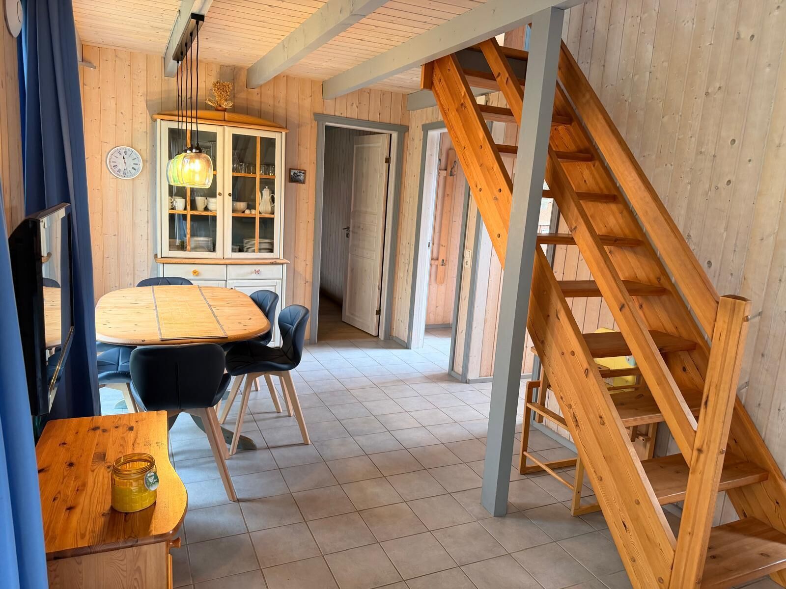 Ein Holzinnenraum mit Essbereich, einer Schranke mit Glastüren und einer Treppe.