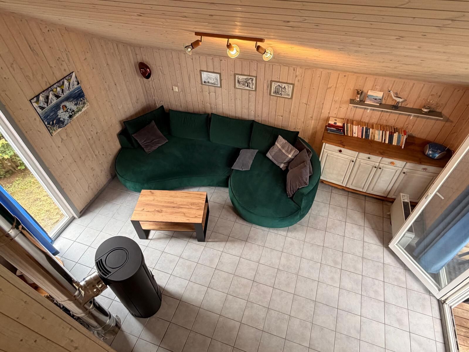 Una habitación acogedora con un sofá verde, una mesa de madera y un cesto de basura.