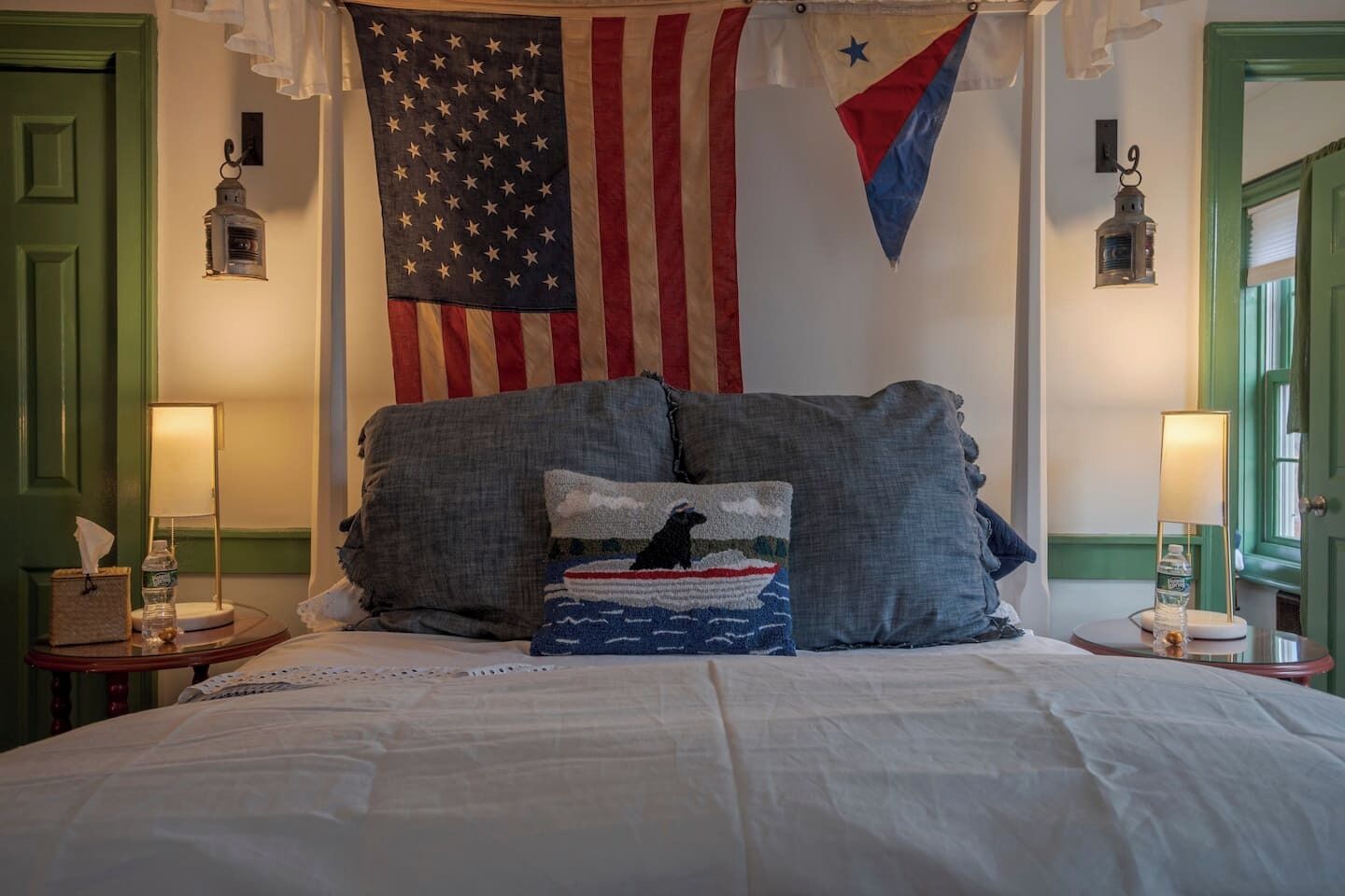 A bedroom with a large bed, two nightstands, a hanging American flag, and a star-spangled pillow.