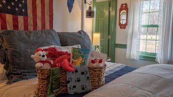 Een netjes opgemaakt bed met een decoratief kussen, een mand met knuffels en een boek, en een ingelijst certificaat op het nachtkastje.
