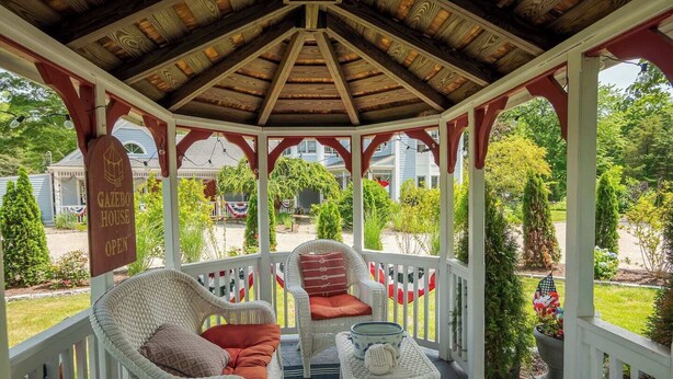 A gazebo with wicker furniture and a sign indicating it's open. - New England Hospitality at the Carriage House
Mystic Vacation Rentals LLC (Old Mystic)