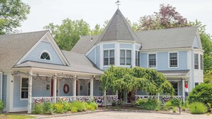 A large, two-story house with a wrap-around porch, a prominent chimney, and a flag on the right side. - New England Hospitality at the Carriage House
Mystic Vacation Rentals LLC (Old Mystic)