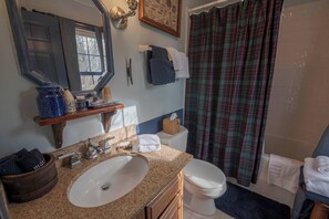 A bathroom with a granite sink, white toilet, and a shower with plaid curtains.