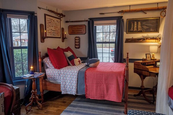 A cozy bedroom with a wooden bed, a desk with a lamp, and a window with curtains.