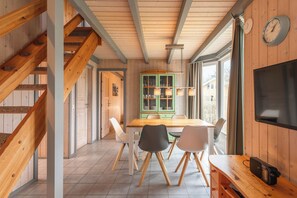 Een houten interieur met een eethoek, een trap en een aan de muur bevestigde televisie.