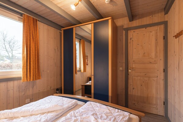 Een slaapkamer met een groot bed, een houten garderobe, een spiegel en een raam met gordijnen.