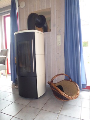 Una habitación con pared revestida de madera, estufa blanco y negro, una cesta de mimbre y una silla.