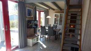 A spacious living area with a dining table, chairs, a TV, and a staircase. - Wildgans 273 - Klassisches Skandinavisches Ferienhaus für bis zu 6 Personen (Mirow)