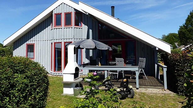 A house with a sloped roof, a chimney, and a patio with a table and chairs. - Wildgans 273 - Klassisches Skandinavisches Ferienhaus für bis zu 6 Personen (Mirow)