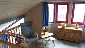 A room with a wooden ceiling, a wooden chair, a small table with a vase of flowers, and a wooden cabinet with decorative items. - Wildgans 273 - Klassisches Skandinavisches Ferienhaus für bis zu 6 Personen (Mirow)