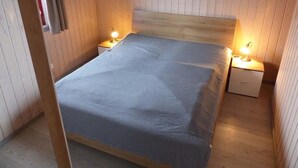 A small, cozy bedroom with a wooden headboard, a single bed, two bedside tables with lamps, and a wall-mounted painting. - Wildgans 273 - Klassisches Skandinavisches Ferienhaus für bis zu 6 Personen (Mirow)