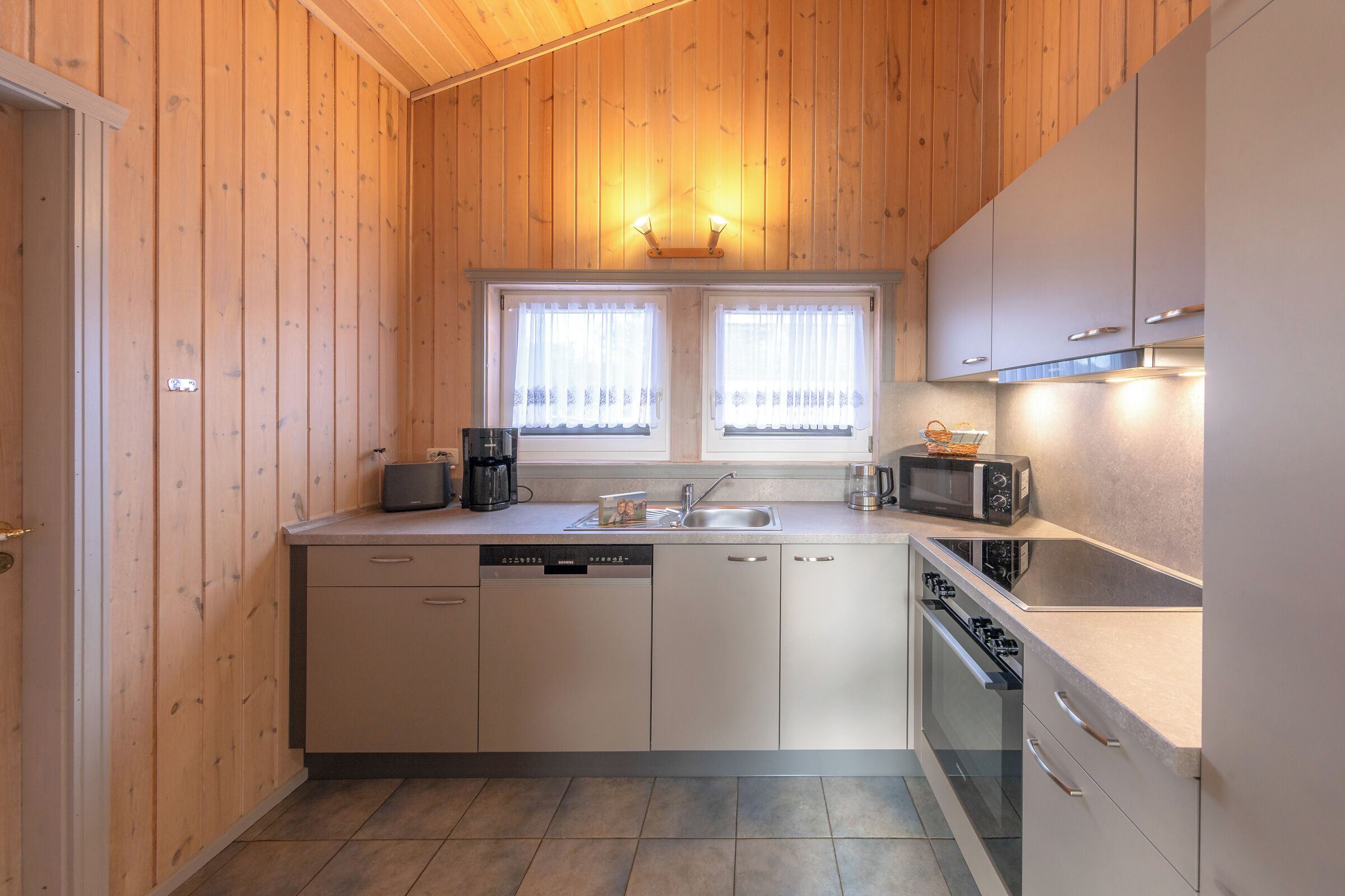 Een kleine keuken met houten wanden, een inbouwvaatwasser, een magnetron en een fornuis.