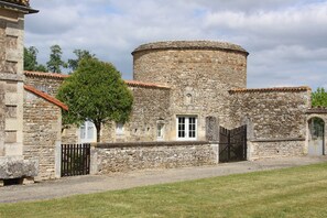 Un edificio de piedra con una torre redonda, una entrada y un árbol frente a él.