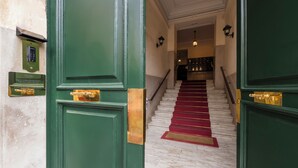 Una imponente escalera con alfombra roja que conduce a un rellano, flanqueada por puertas verdes con tiradores de latón.