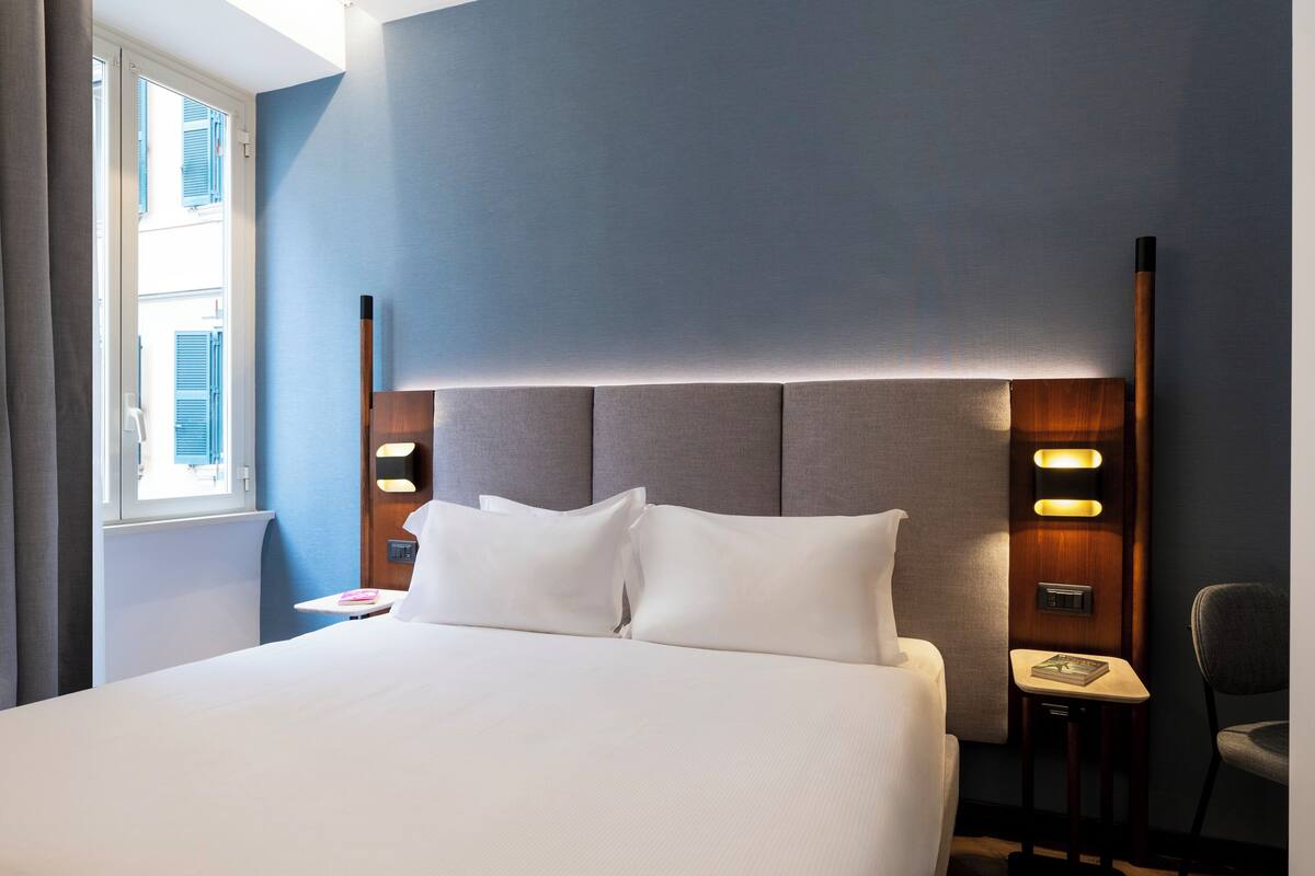 A neatly made bed with a headboard, bedside lamps, and a small table with a book.