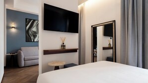 Una habitación de hotel moderna con una cama grande, un televisor de pantalla plana en la pared, una mesita redonda pequeña, un sofá y un espejo.