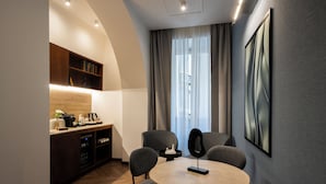 Una habitación de hotel moderna con una mesa de comedor redonda, sillas grises, una cafetera y una estantería.