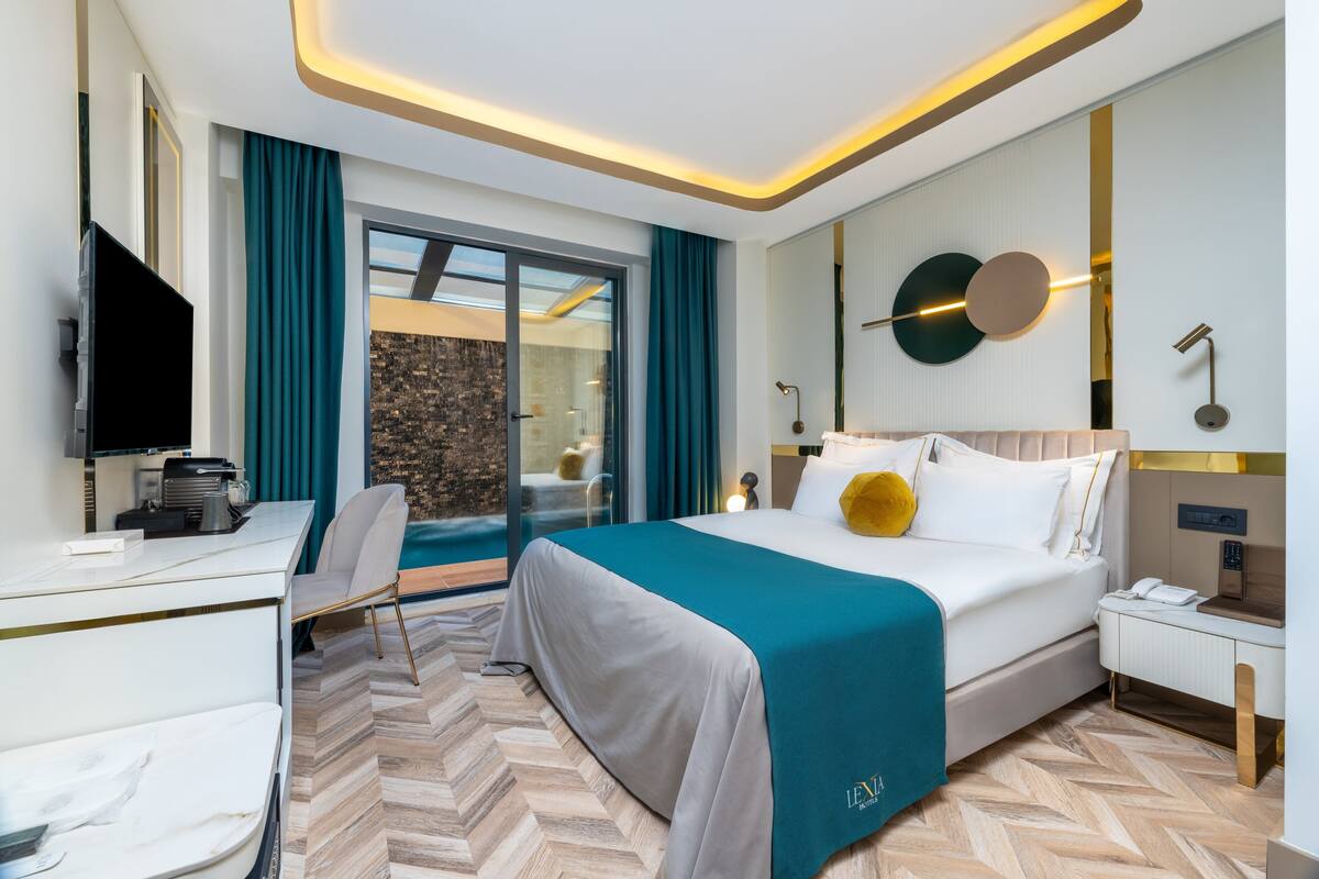 A modern hotel room with a bed, a desk, a chair, a TV, and a view of a pool.