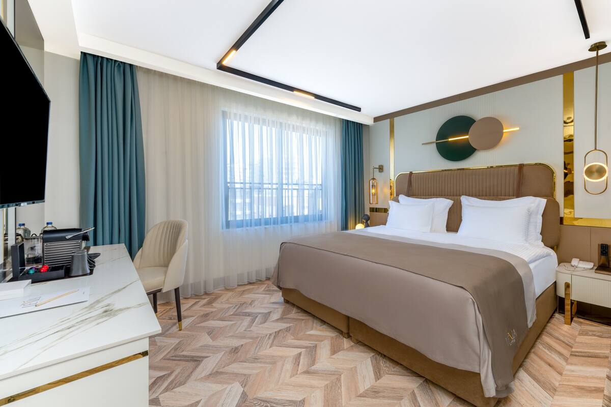 A modern hotel room with a large bed, a desk with a computer, and a window with curtains.