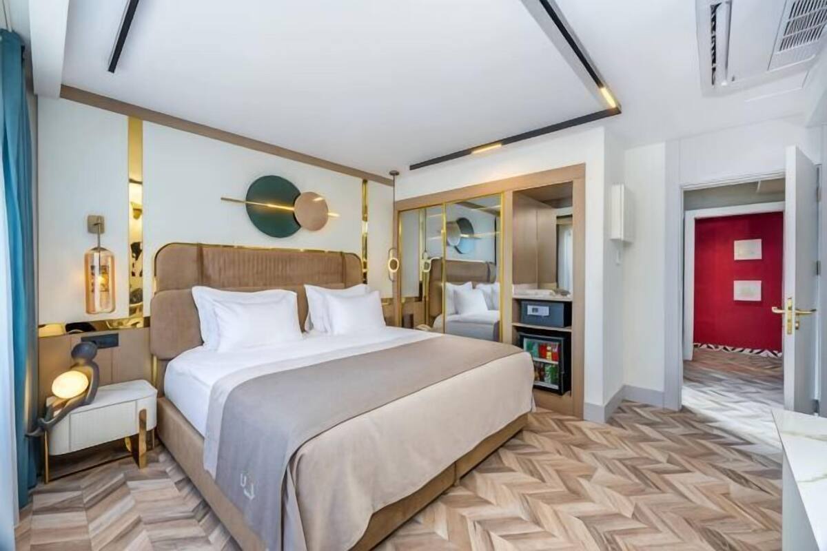 A modern hotel room with a large bed, bedside tables, a mirror, and a red door.