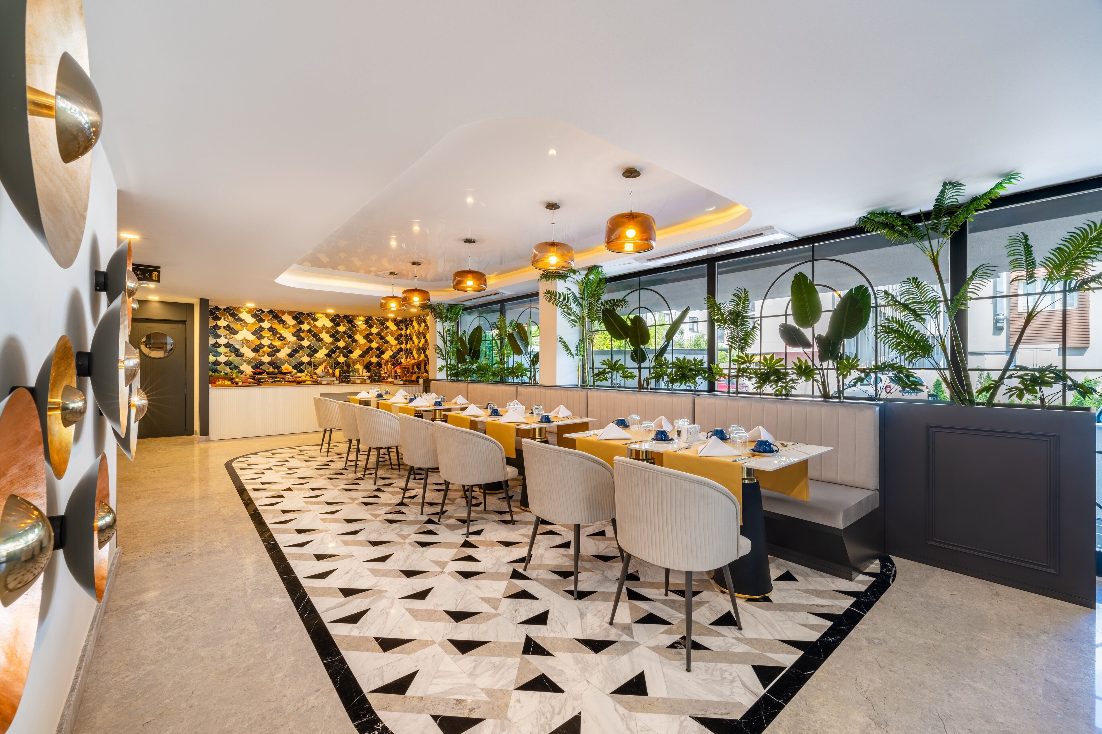 A modern restaurant with a geometric patterned floor, multiple dining tables with chairs, pendant lighting, and a view of greenery through large windows.