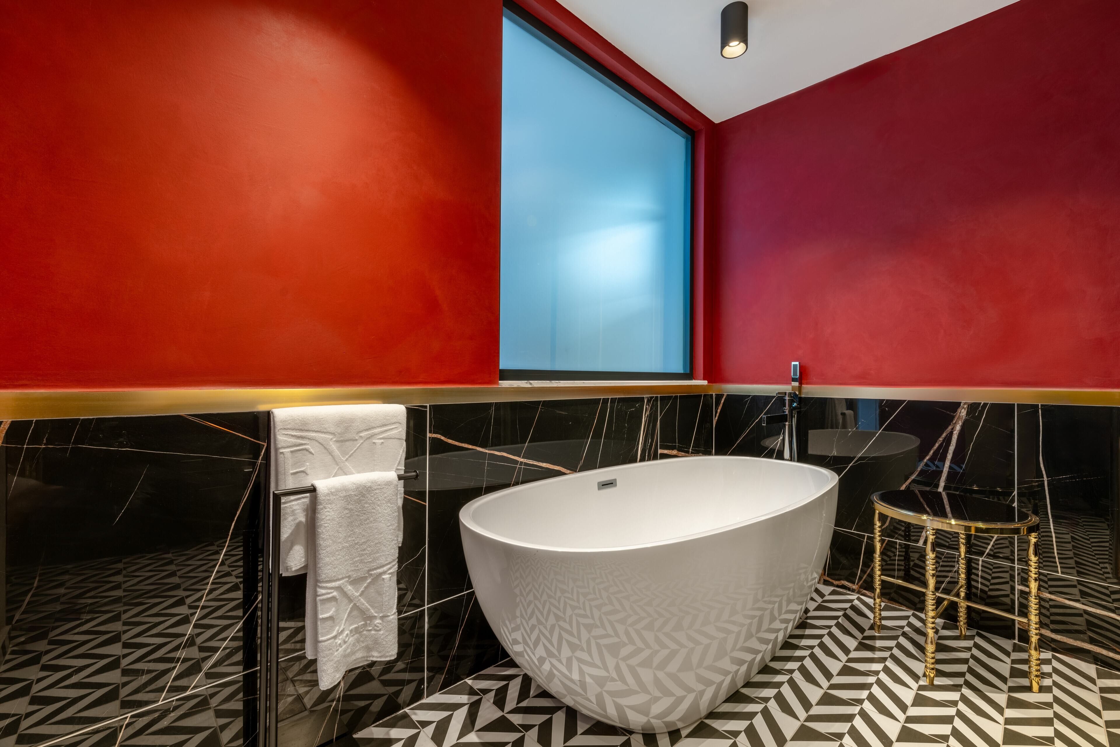 A modern bathroom with a freestanding bathtub, black and white patterned floor, red walls, and a large window.