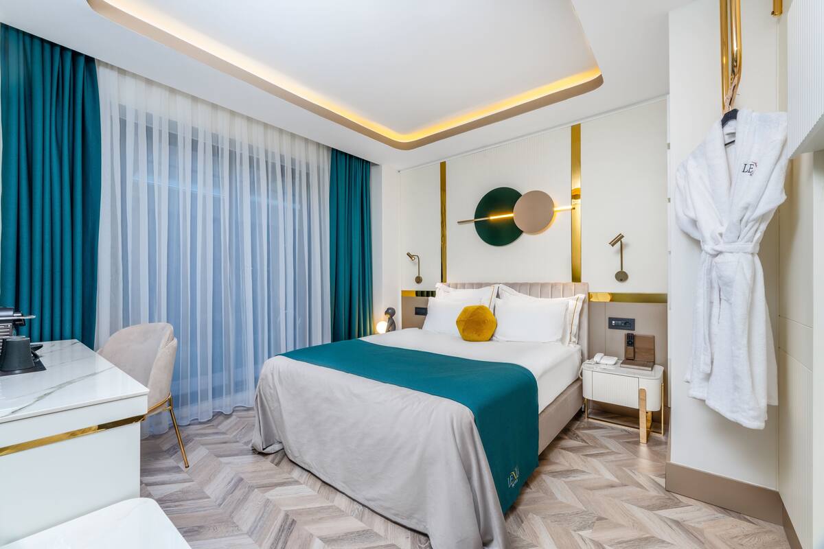 A modern hotel room with a large bed, a desk, and a robe hanging on the wall.