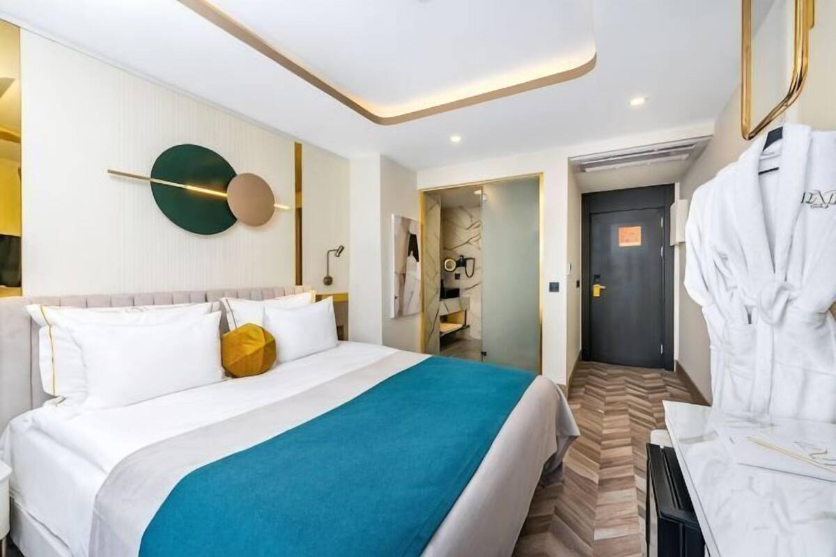 A hotel room with a bed, a robe, a mirror, and a door.