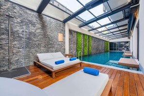 Una habitación moderna con piscina envuelta en cristal, suelo de madera, cama con toallas azules y pared de piedra.
