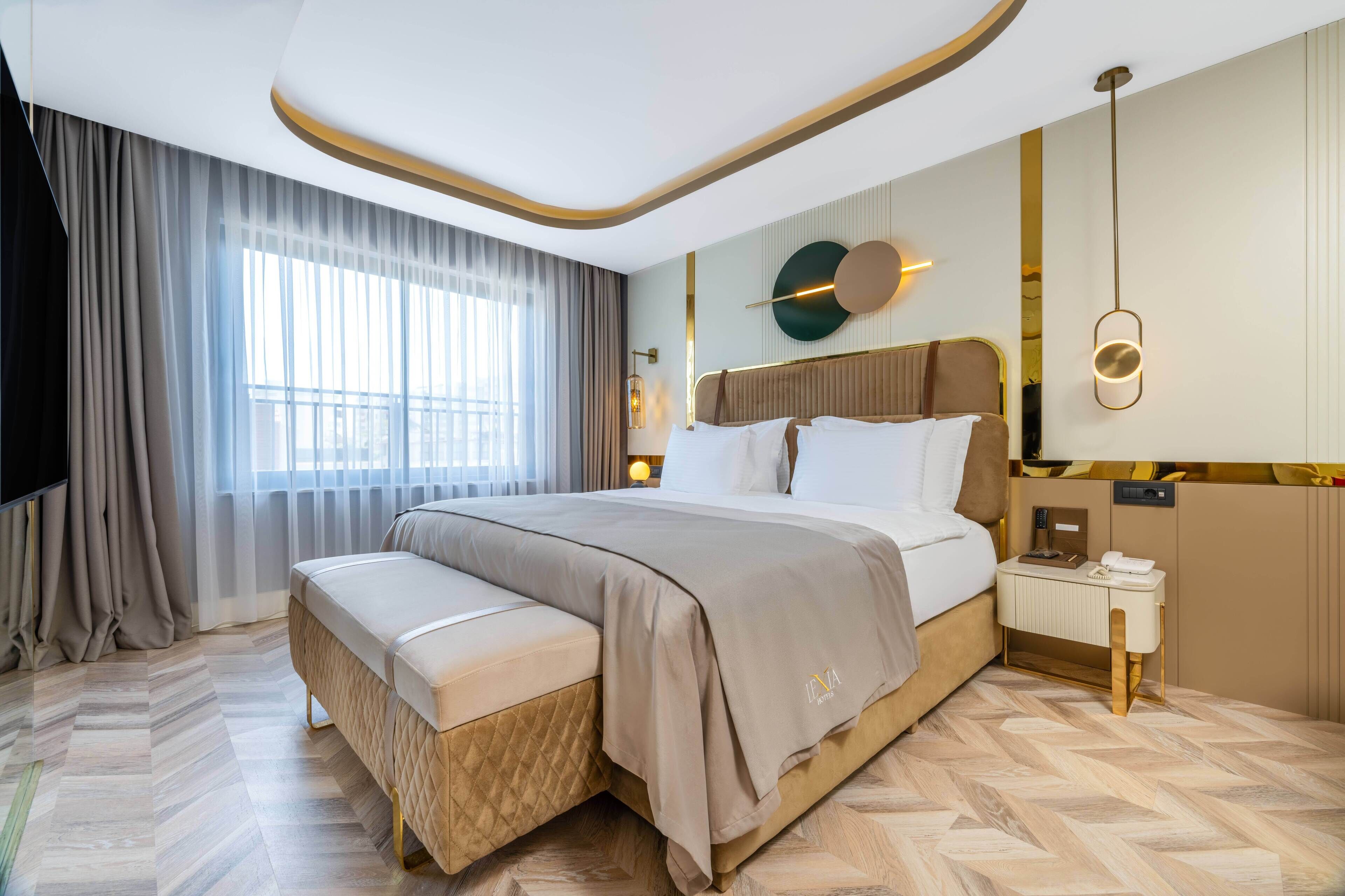 Una habitación de hotel moderna con una cama grande, un banco, una mesita de noche y un televisor montado en la pared.