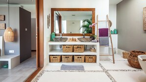 Un baño moderno con un espejo grande, cestas de mimbre, una escalera de madera y un lavabo con un recipiente amplio.