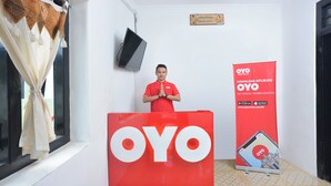 A hotel reception area with a large red OYO sign, a television mounted on the wall, and a promotional banner for OYO Hotels. - OYO 634 Elga Sastro Inn Syariah (Yogyakarta)