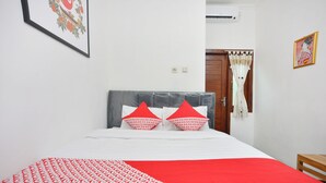 A neatly made bed with a patterned bedspread and two pillows, a wooden chair, and a door with a curtain. - OYO 634 Elga Sastro Inn Syariah (Yogyakarta)