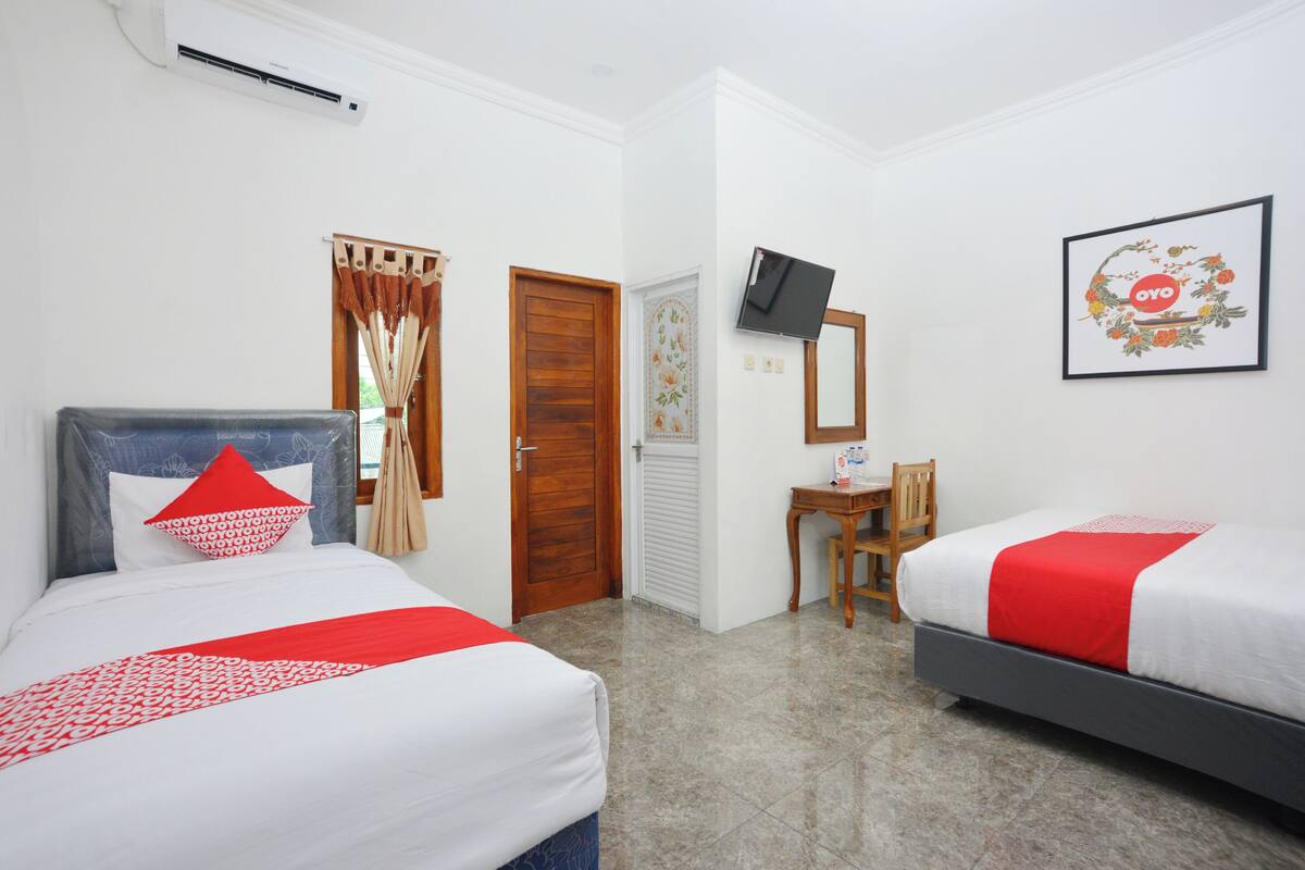 Ein Hotelzimmer mit zwei Betten, einem Schreibtisch, einem Fernseher und einem gerahmten Bild an der Wand.