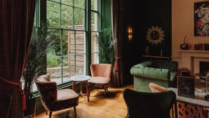 Une pièce chaleureuse avec un canapé vert, un fauteuil à motifs et une petite table ronde.
