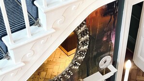 Une cheminée surmontée d’un miroir, un plancher en bois et un escalier avec des rampes blanches.