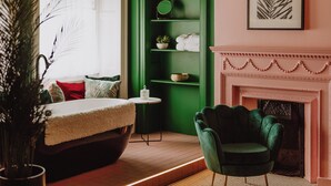Une pièce chaleureuse avec un mur d’accent vert, une cheminée, un fauteuil confortable et une petite table agrémentée d’une plante.