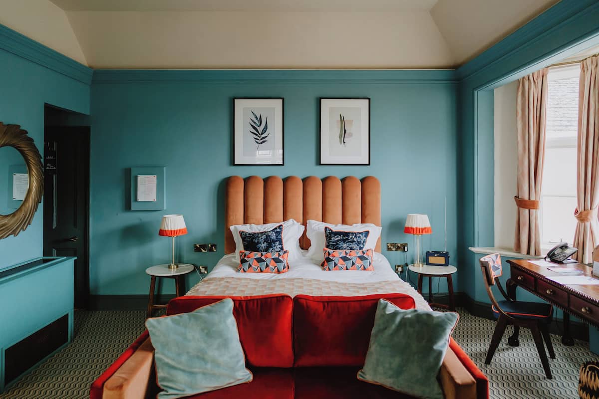 A hotel room with a large bed, two framed pictures on the wall, a desk with a chair, and a window with curtains.