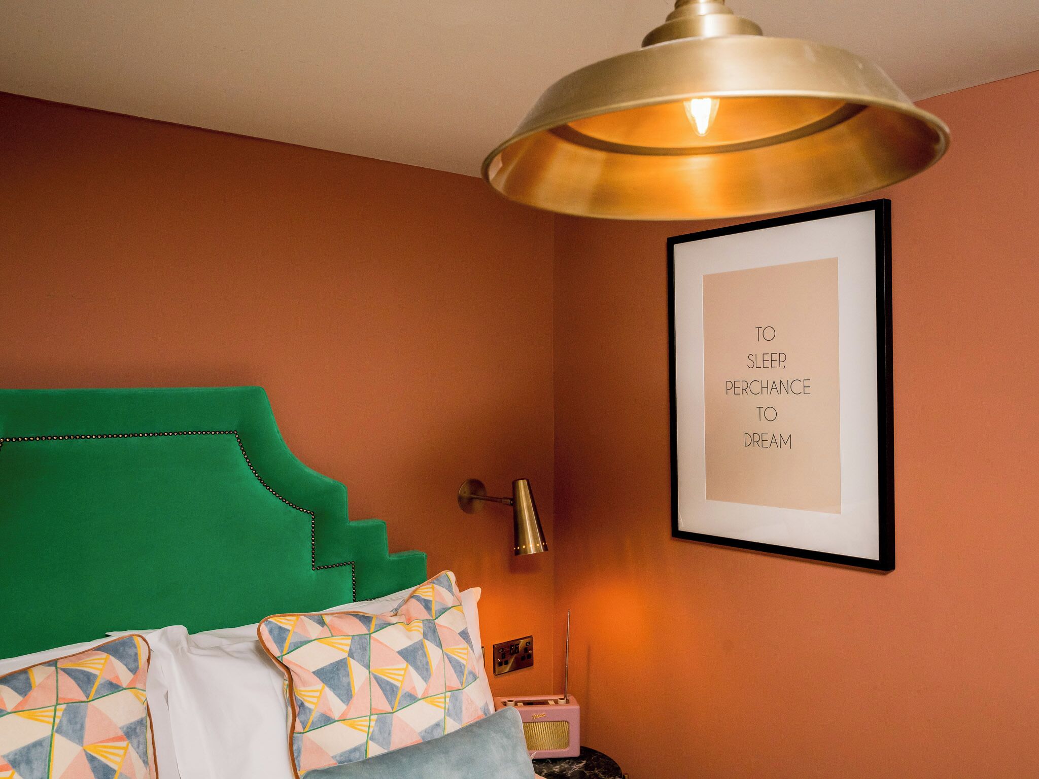 A bedroom with a green headboard, a framed inspirational quote on the wall, and a bedside lamp.