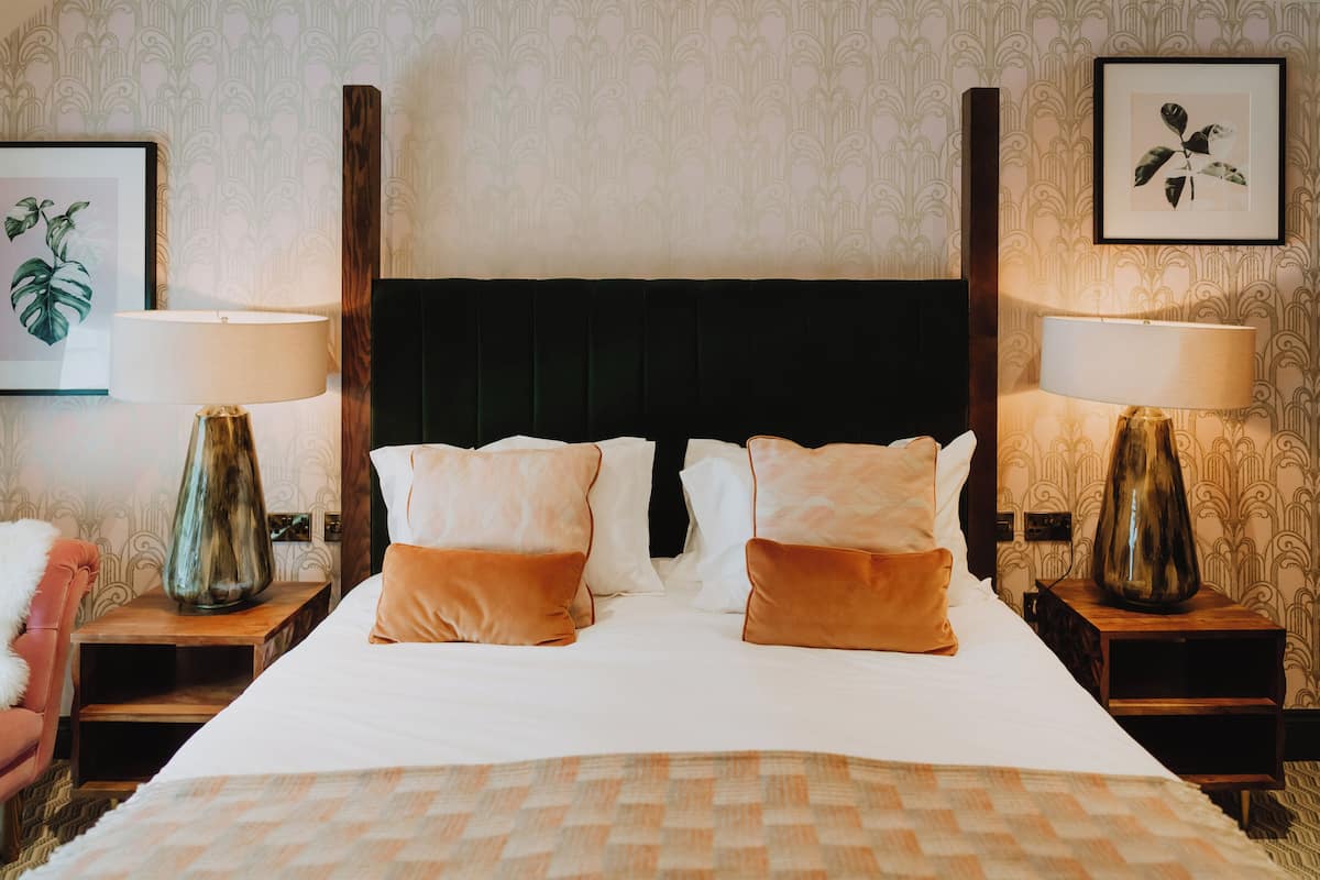 A neatly made bed with a patterned bedspread, flanked by two bedside tables with lamps and framed artwork on the walls.