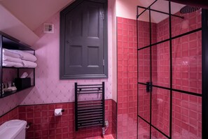A bathroom with a red tiled shower, a black towel rack, a white toilet, and a towel shelf. - Ingleside House (Cirencester)