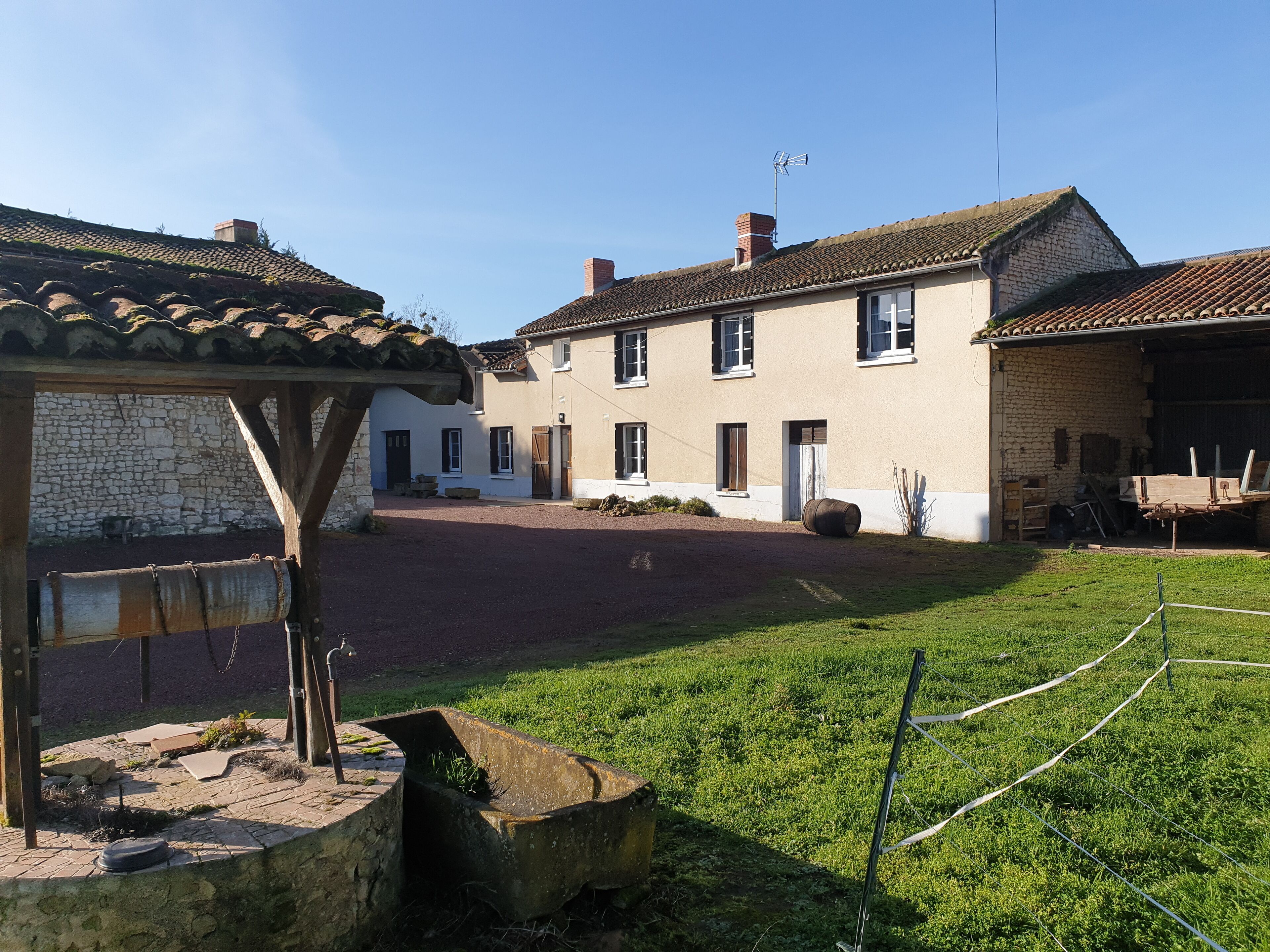 A traditional stone building with a tiled roof, a covered outdoor seating area, and a grassy courtyard.