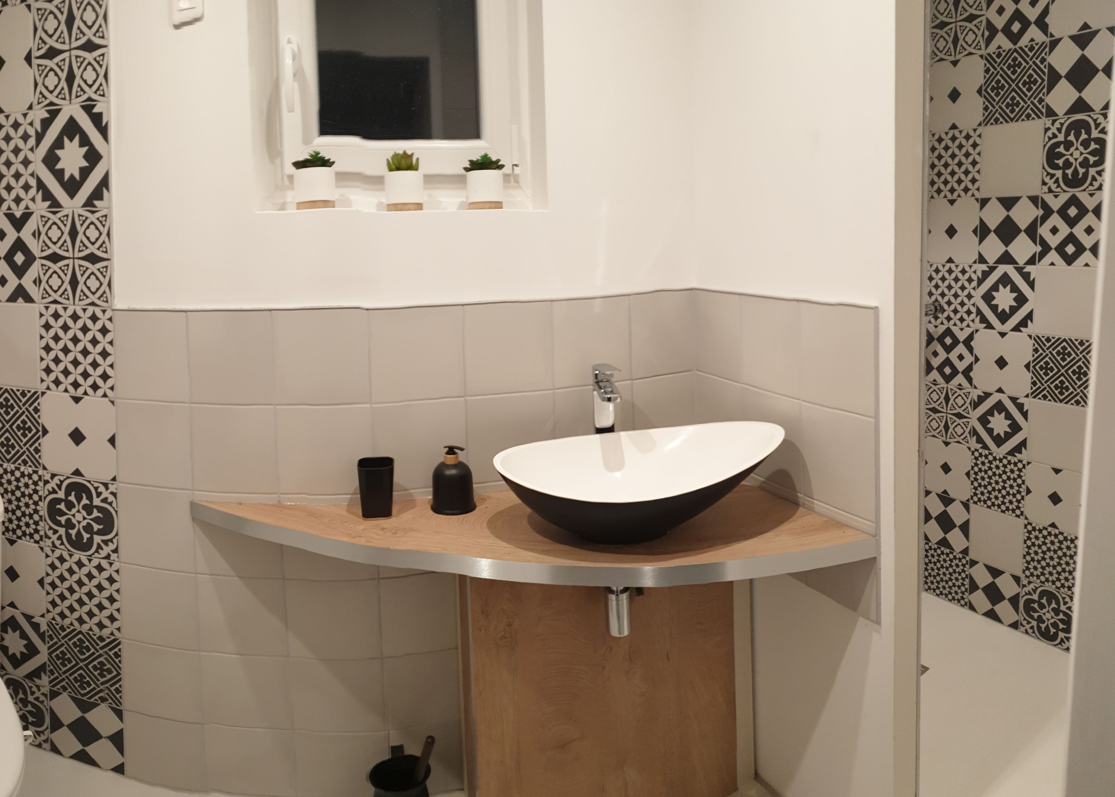 Een badkamer met een moderne wastafel, een raam boven de wastafel en patroontegels op de muren.